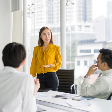 Zelfverzekerde zakenvrouw geeft presentatie in bestuurskamer. Professionals zijn in vergadering aan de vergadertafel. Ze delen ideeën op kantoor.