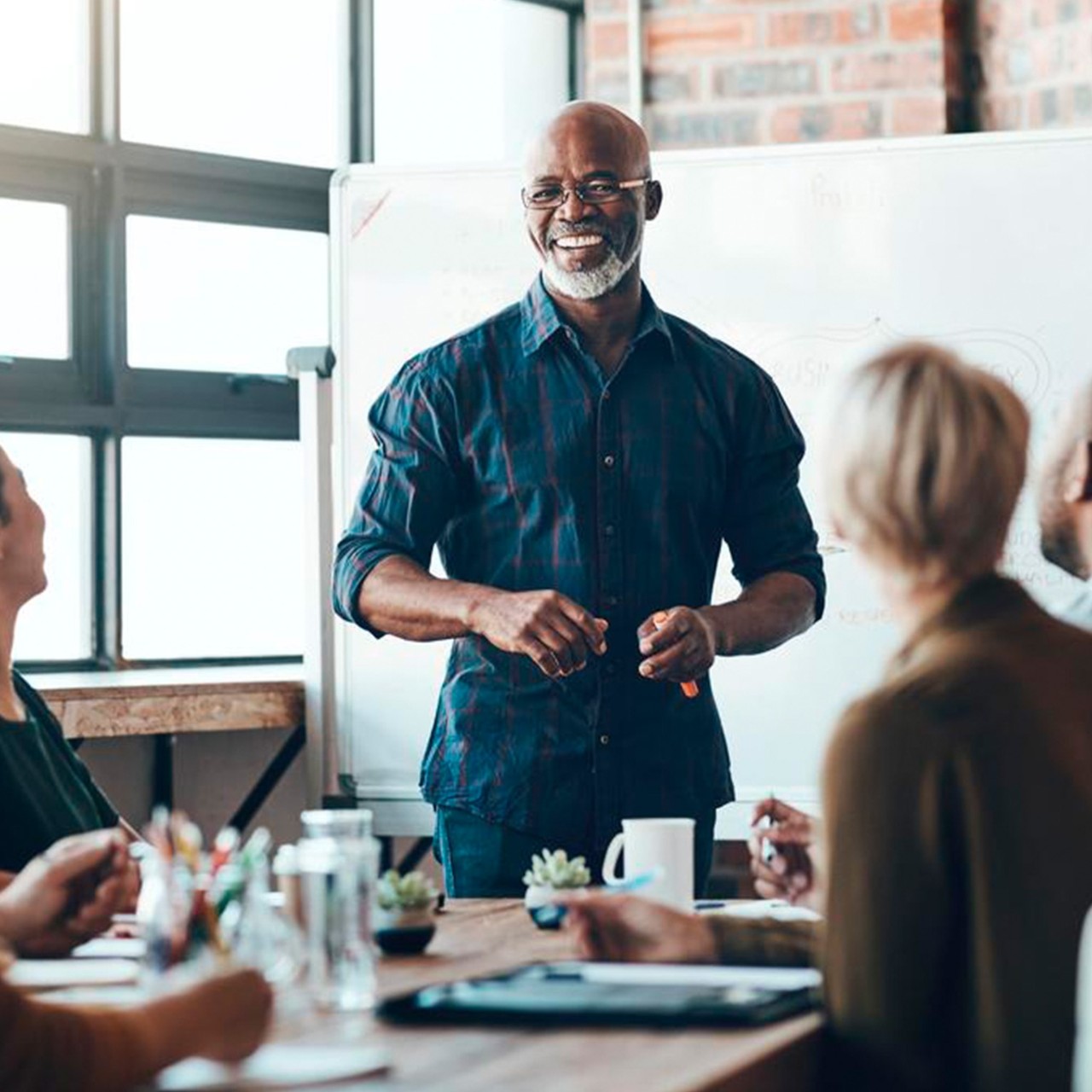 A senior man leads a discussion in a well-lit conference room filled with professionals.