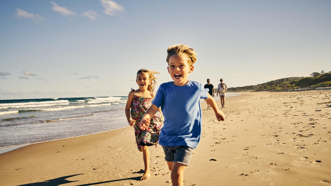 two adorable little children running at the beach with their parents