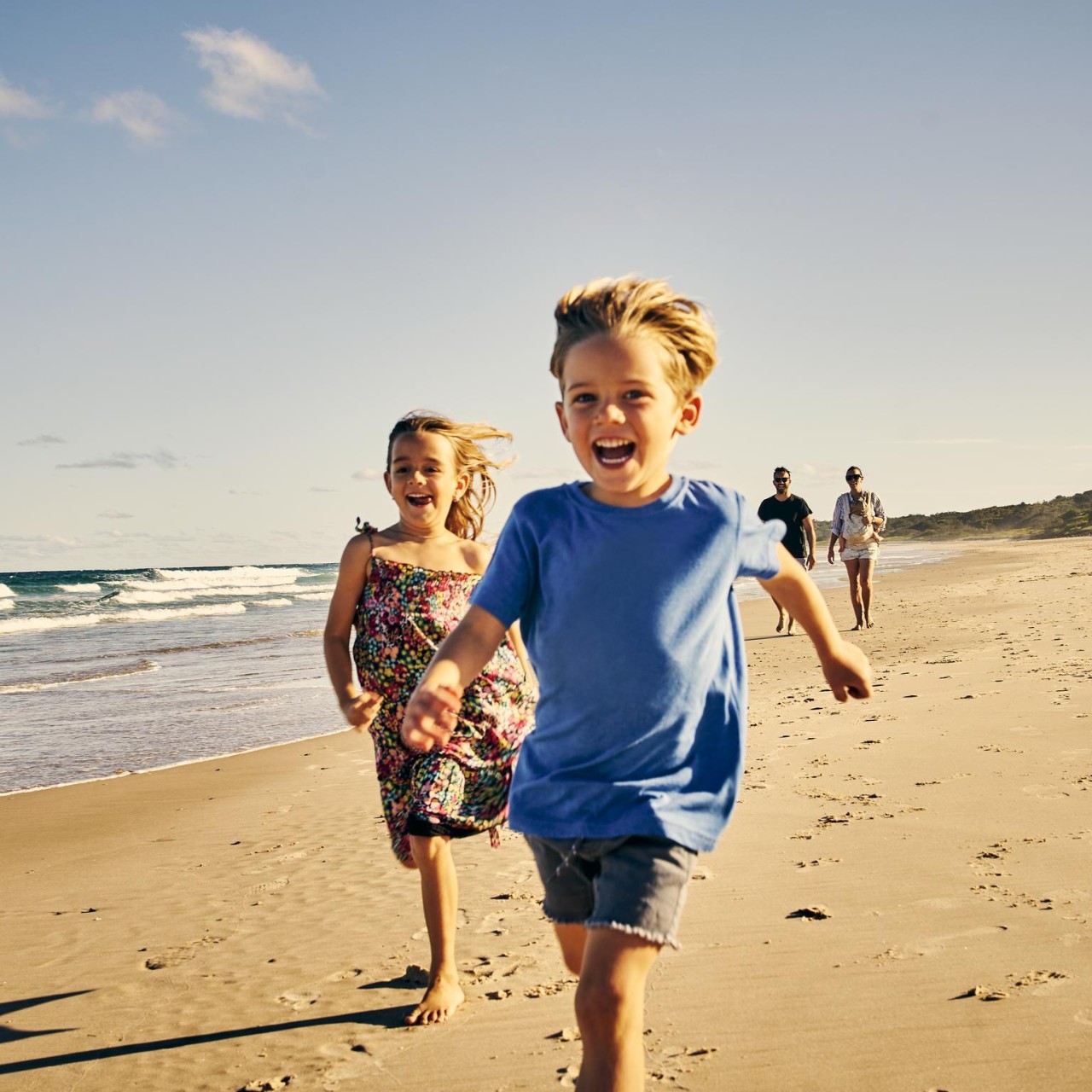 two adorable little children running at the beach with their parents