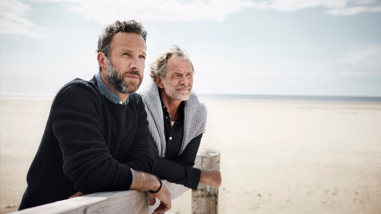 Two mature men leaning on railing of boardwalk on the beach