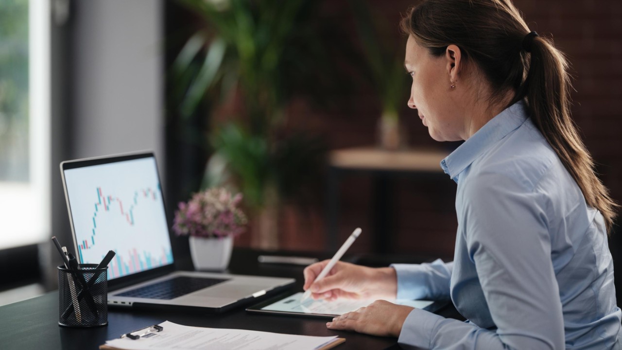 woman-on-laptop-and-cell-phone-with-data-printouts