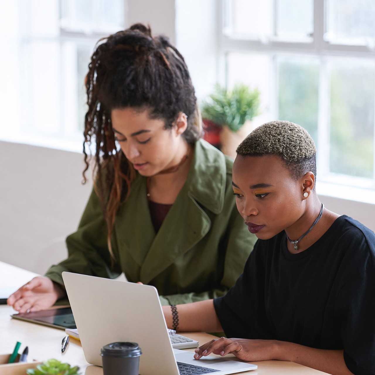 College students working together two young women friends brainstorming ideas for project sitting at desk using laptop computer in class